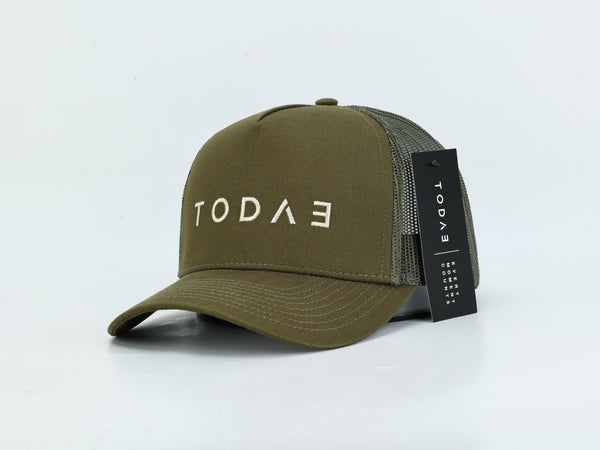 An olive green trucker cap with a curved brim, featuring the brand name 'TODAE' embroidered in white on the front. The back of the cap is made of olive green mesh, and a black hangtag with the brand name is attached.