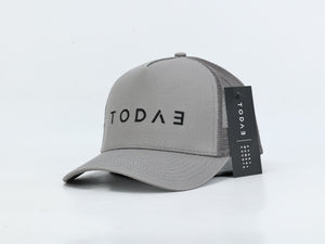 A light gray trucker cap with black mesh back panels and a black hangtag, featuring the brand name 'TODAE' printed on the front.